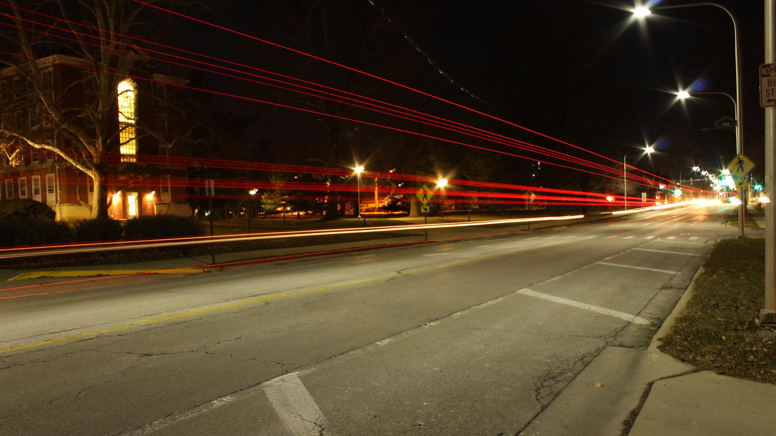 A street and University of Illinois campus buildings at night. Red lines show where car tail lights passed by.