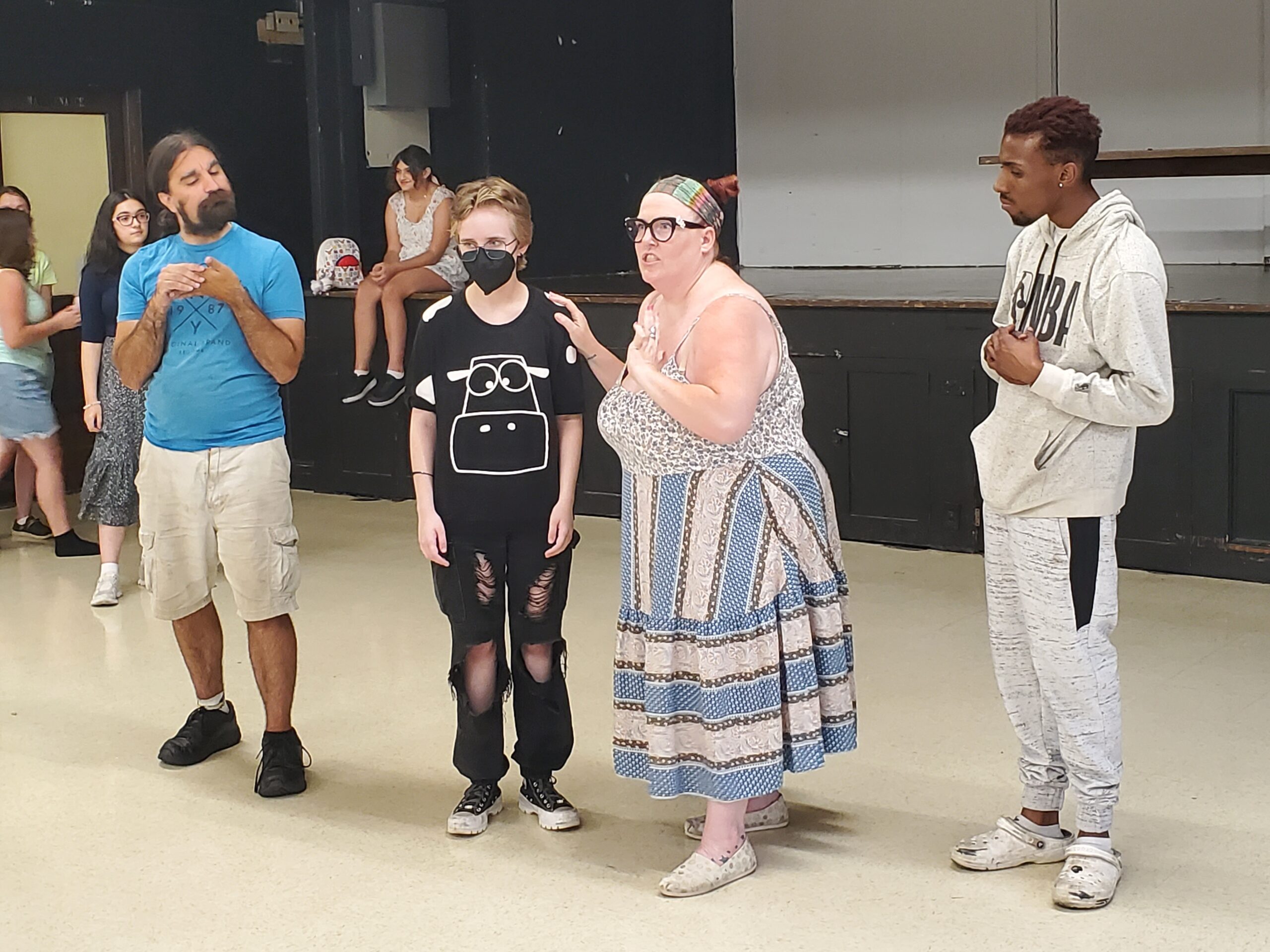 Four individuals stand in front of a stage, looking concerned. They are rehearsing Shakespeare's tragedy "Titus Andronicus."