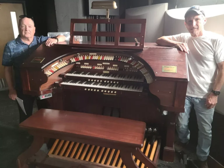 Two men stand on opposite sides of a Wurlitzer organ