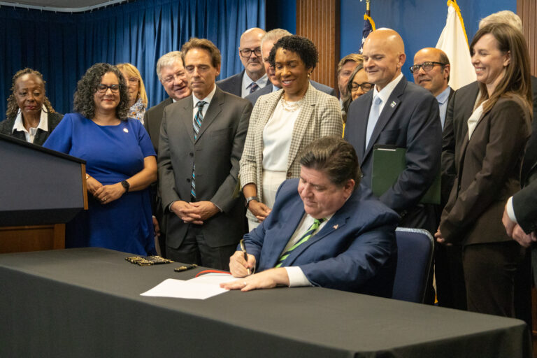 Lawmakers surround Illinois governor as he signs a bill.
