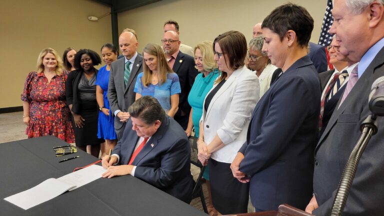 Crowd surrounds Gov. Pritzker signing a bill into law.