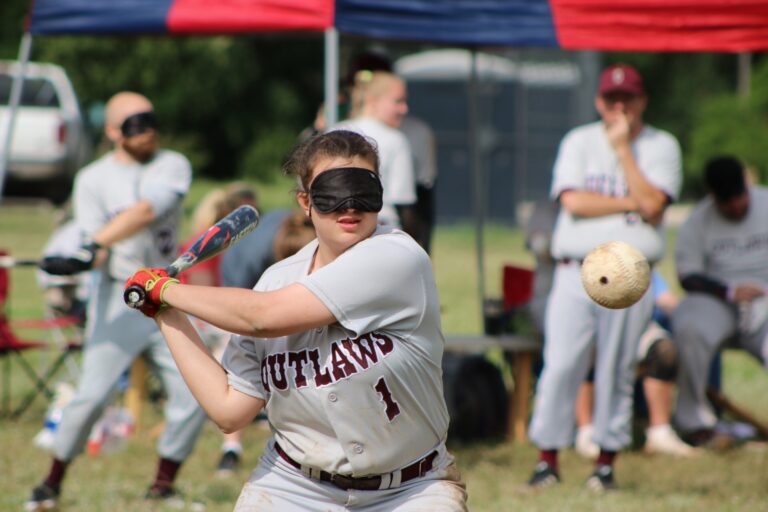 A baseball player wears an eye mask while swinging at bat at a ball.