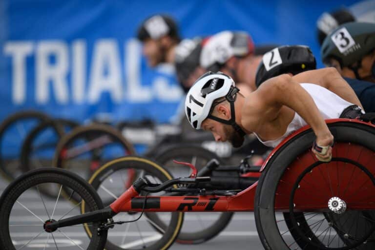 A man in a racing wheelchair leans forward before pushes around a track.