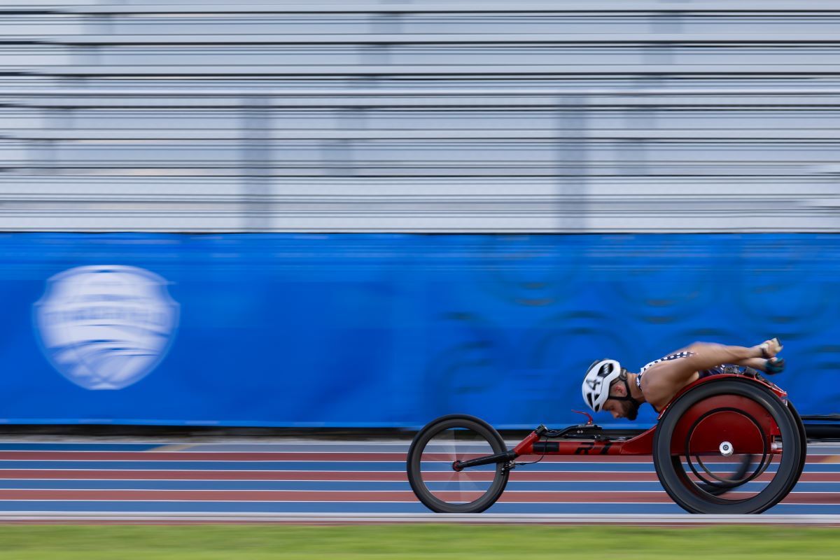 A man in a racing wheelchair pushes around a track.