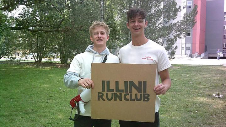 two college students hold a sign that reads "Illini Run Club"