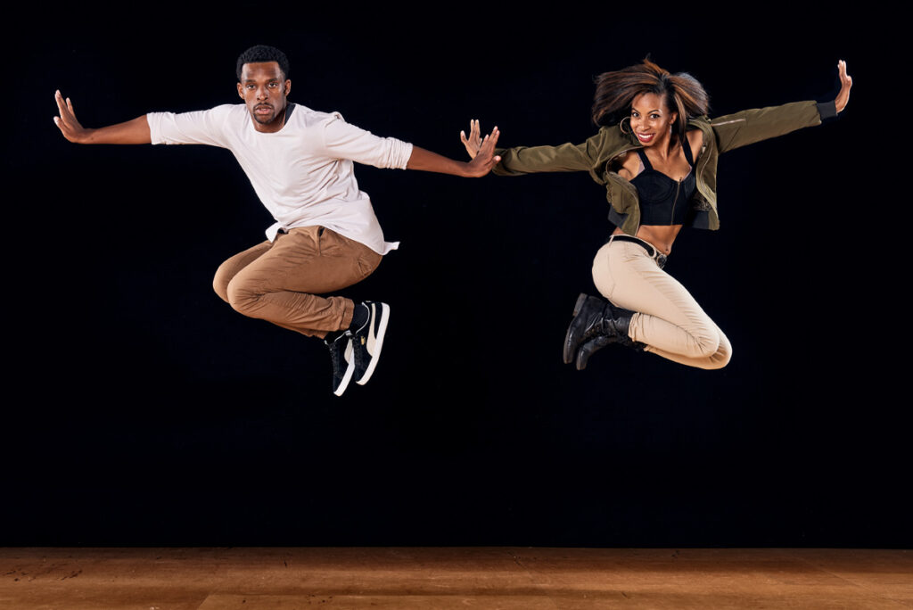 Two people jump and pose in the air with their arms outstretched.