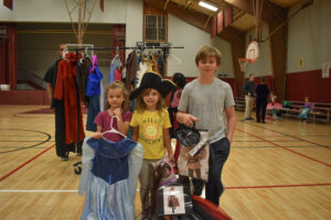 three kids pose holding Halloween costumes