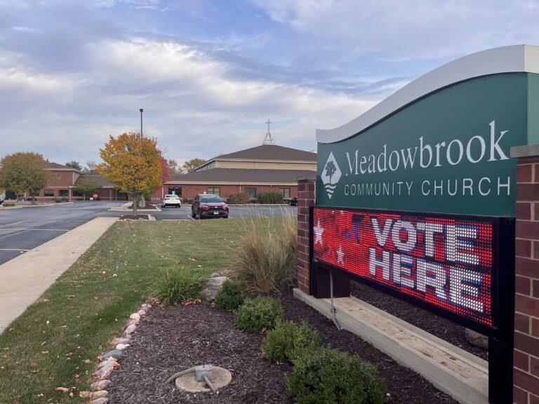 A sign for the Meadowbrook Community Church that says "vote here" below next to a parking lot.