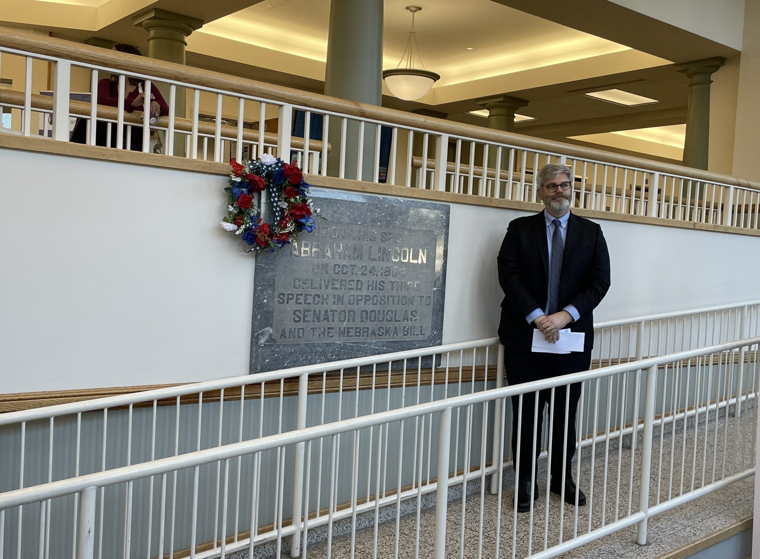 A man stands on a ramp next to a plaque and a wreath commemorating Lincoln's speech against the Kansas-Nebraska Act.