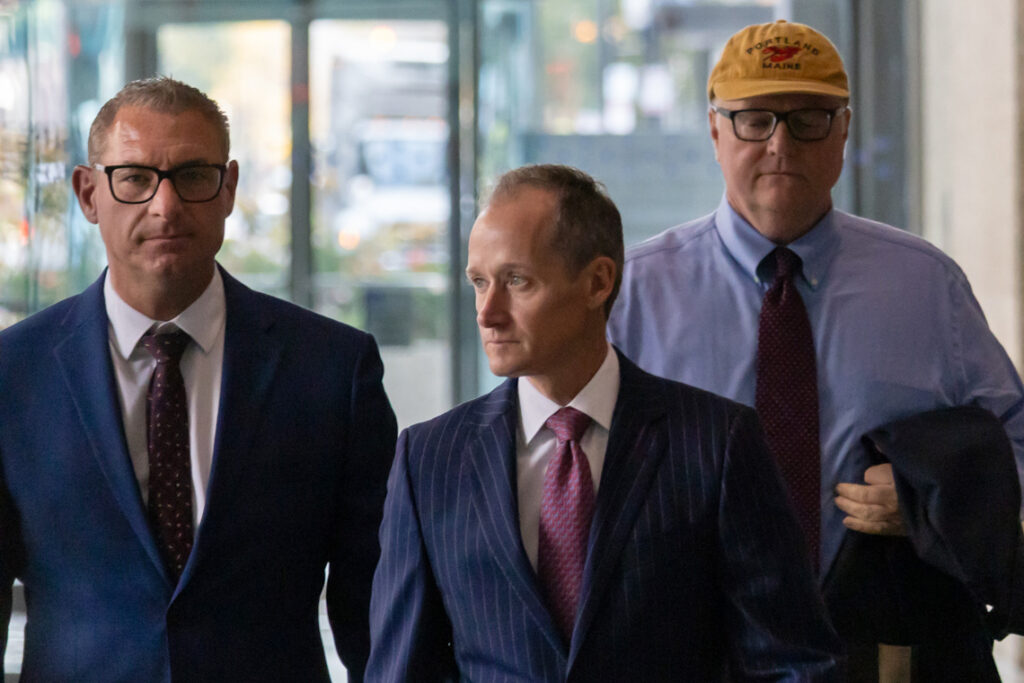 Will Cousineau walks down a hallway with two other men.