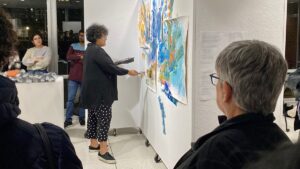 A person painting at an exhibit surrounded by an audience