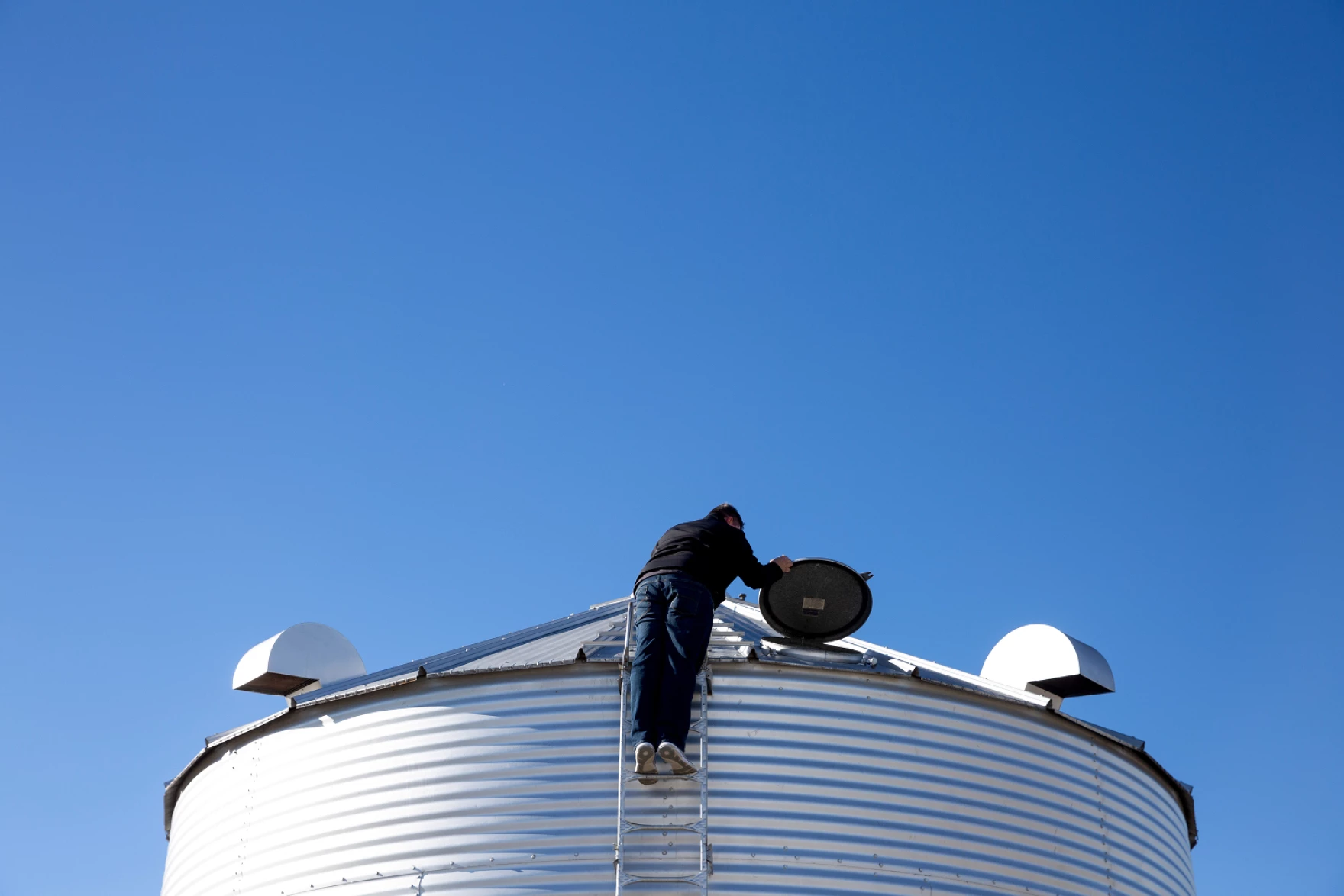 A man stands on a ladder looking from above into a grain bin