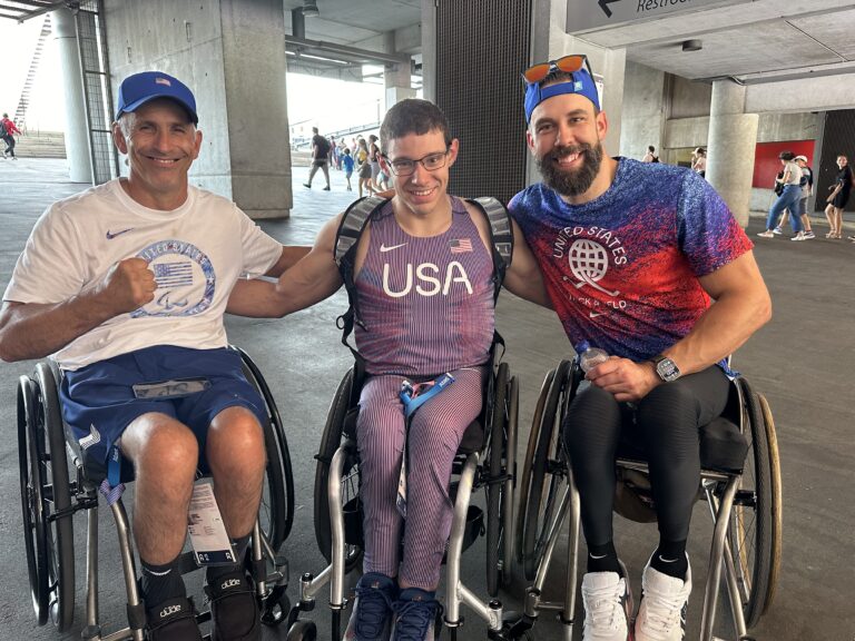 three men in wheelchairs pose for a photo with arms around each other