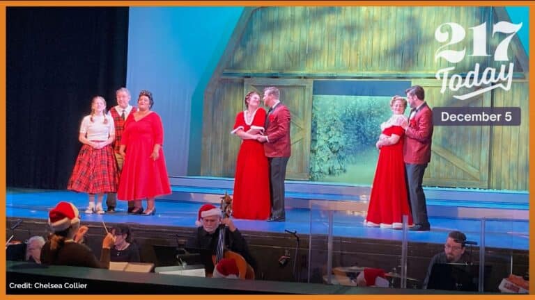 Four people dressed in red pose in front of a tree on a theatre stage.