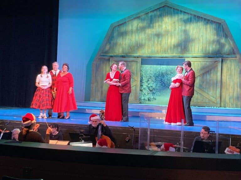 Actors and musicians standing on a stage and in an orchestra pit.