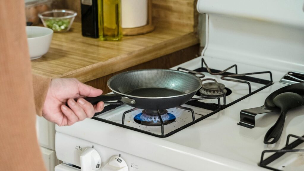 A person heats up a frying pan over a gas stove.