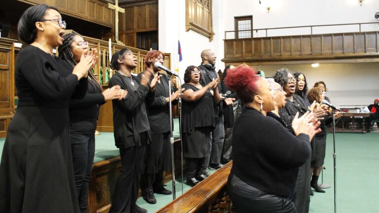 Two rows of singers clap in front of a church altar.