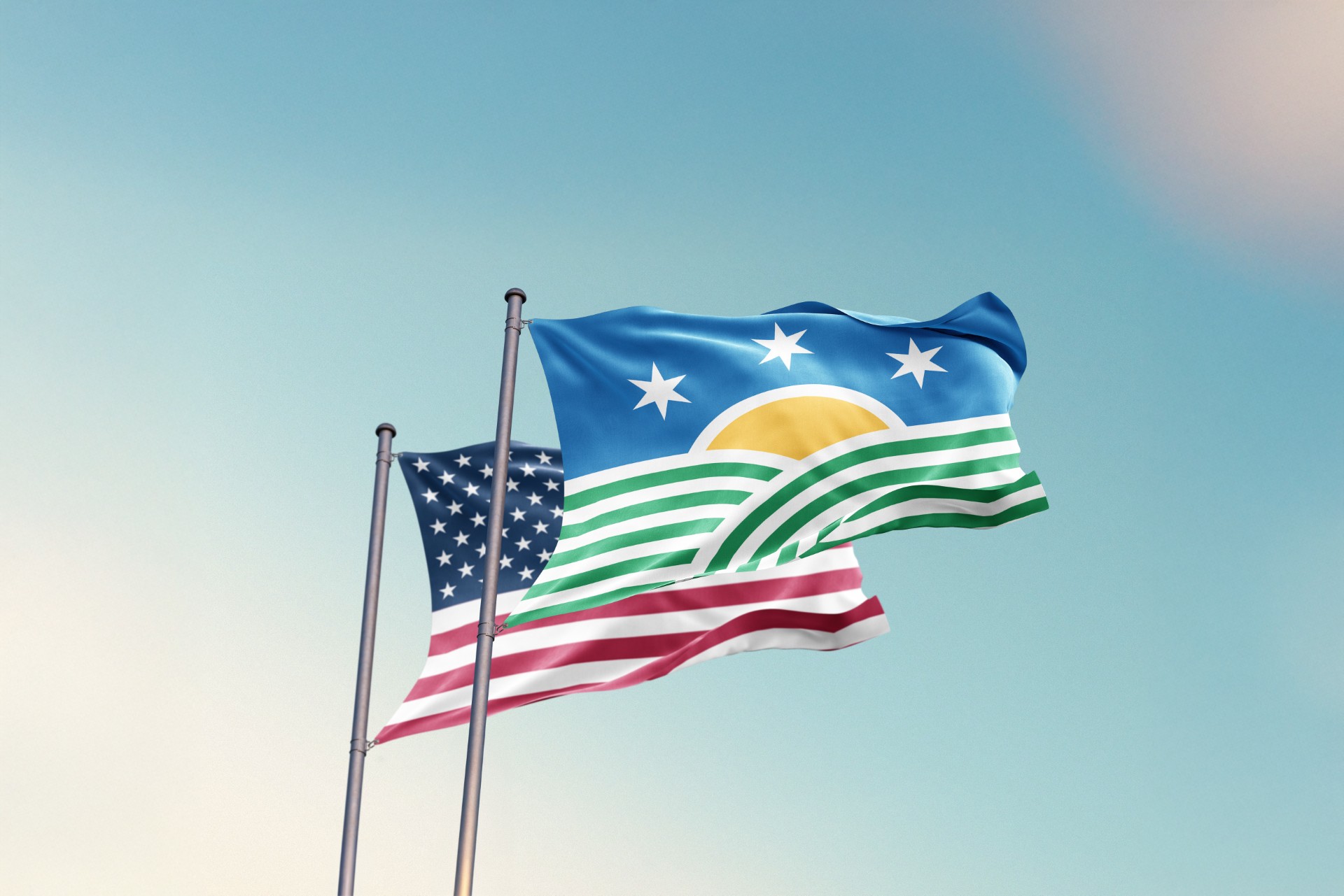 Two flags blow in front of a sky background. One is a flag with a yellow sun in front of a blue background with three stars. Green and white stripes are below the sun. The other is the flag of the United States with 13 red and white stripes and 50 white stars against a blue background.