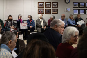 People sit and hold signs that read, "No carbon storage in our drinking water" and "Support local bans. Protect our water."