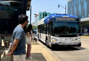 A city bus stopped at a us stop and passengers are standing waiting to get on