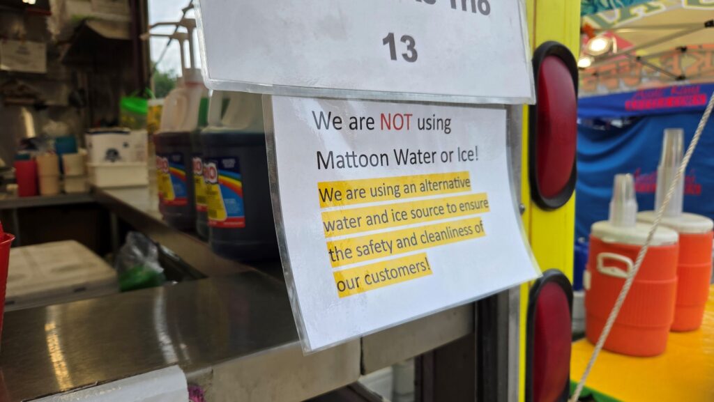 A sign from a vendor reads "We are NOT using Mattoon Water or Ice! We are using an alternative water and ice source to ensure the safety and cleanliness of our customers.