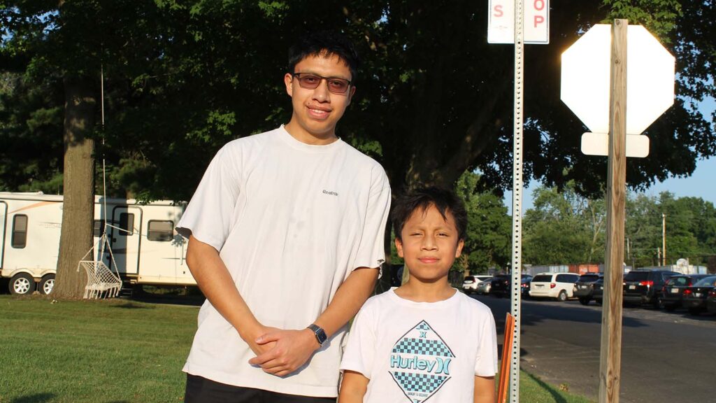 Two brothers stand at a street corner, with trees and street signs behind them.