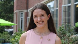 A young woman in a pink dress with a ovary pin stands outside the University YMCA.