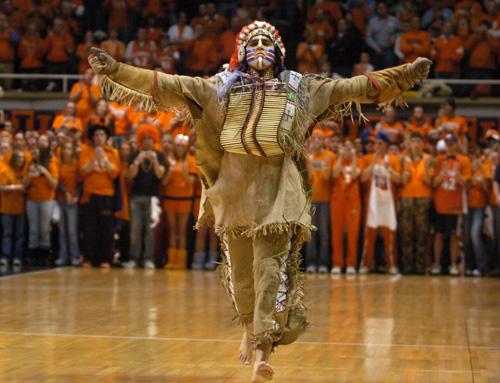 A person dressed as a controversial mascot dances on the floor of a basketball court.