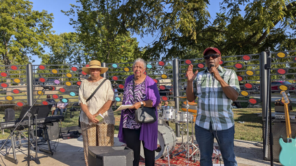 three people stand outside in front of musician tribute wall