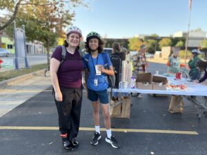 A woman and her son stand in front of a table welcoming cyclists.