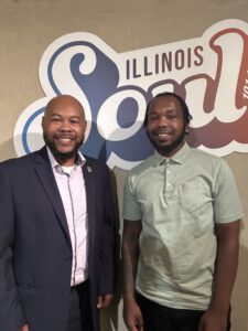 Rantoul Mayor Samuel Hall stands in front of an Illinois Soul banner with his son during a visit to Illinois Public Media's studio.