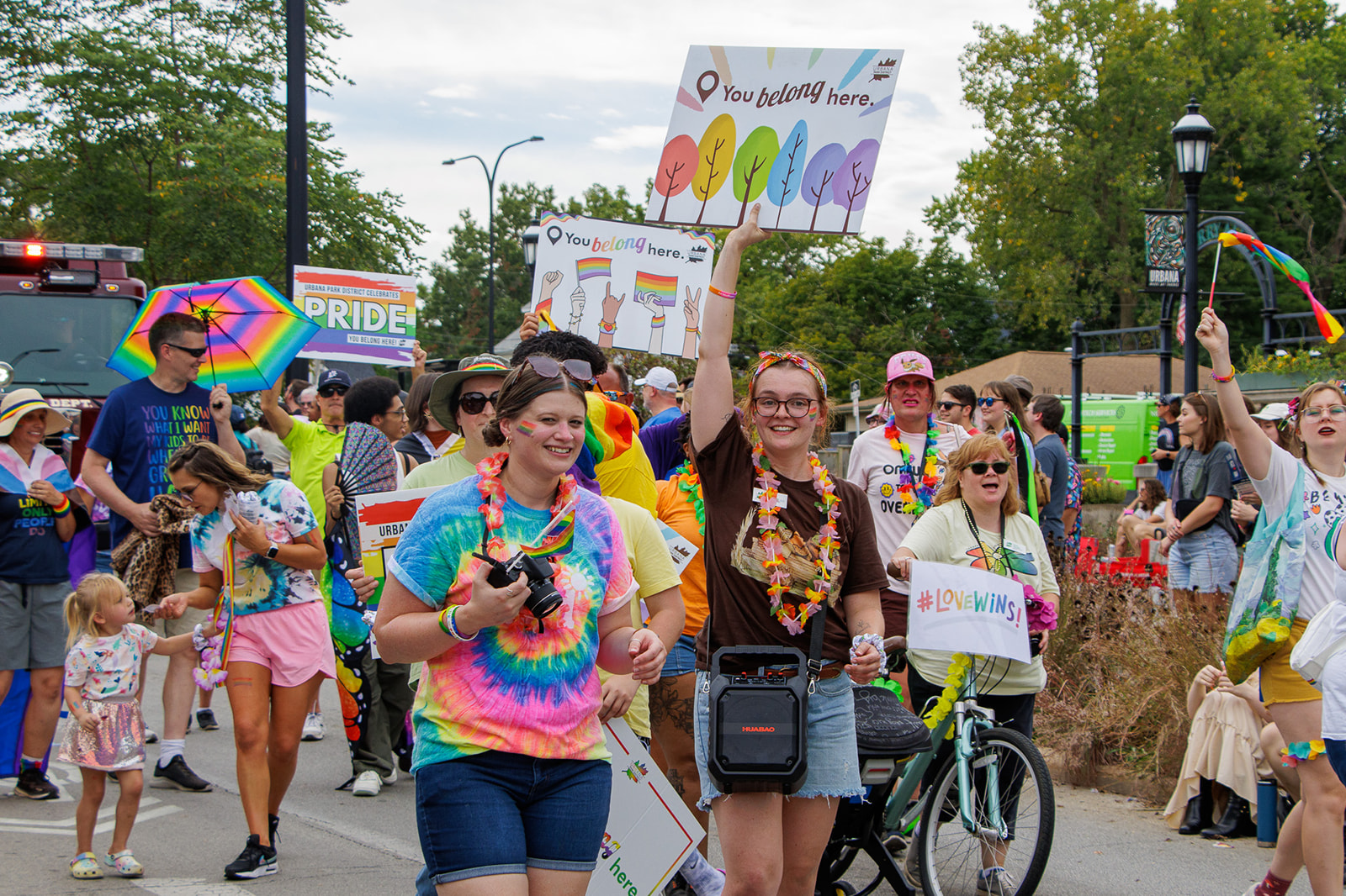 People in brightly colored clothing walk in a parade and hold signs.