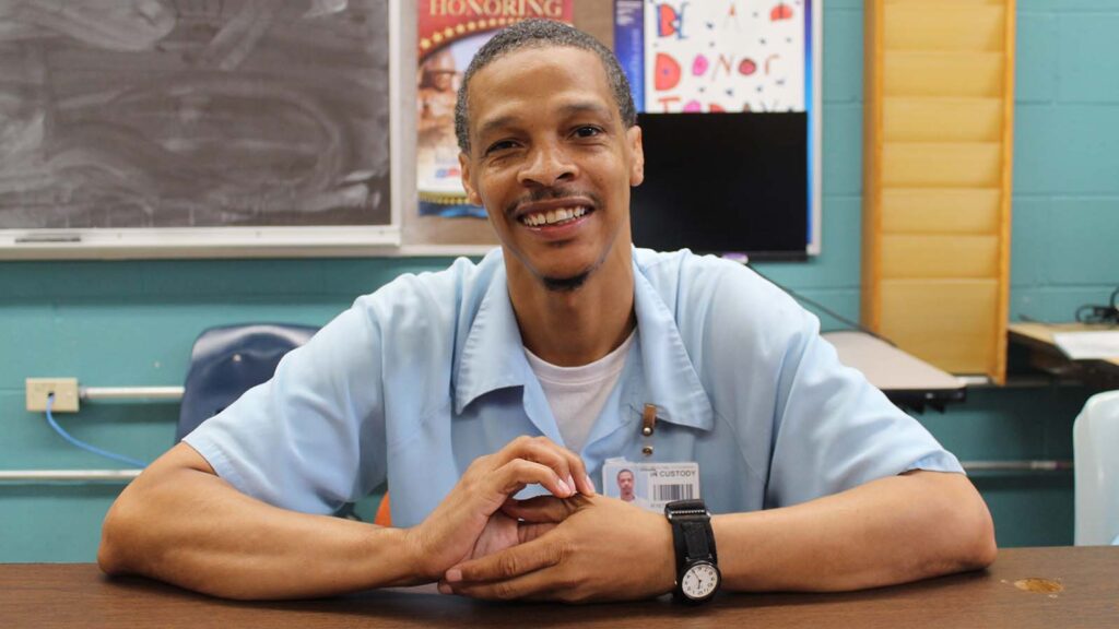 A man with freckles and a watch smiles brightly at the camera.