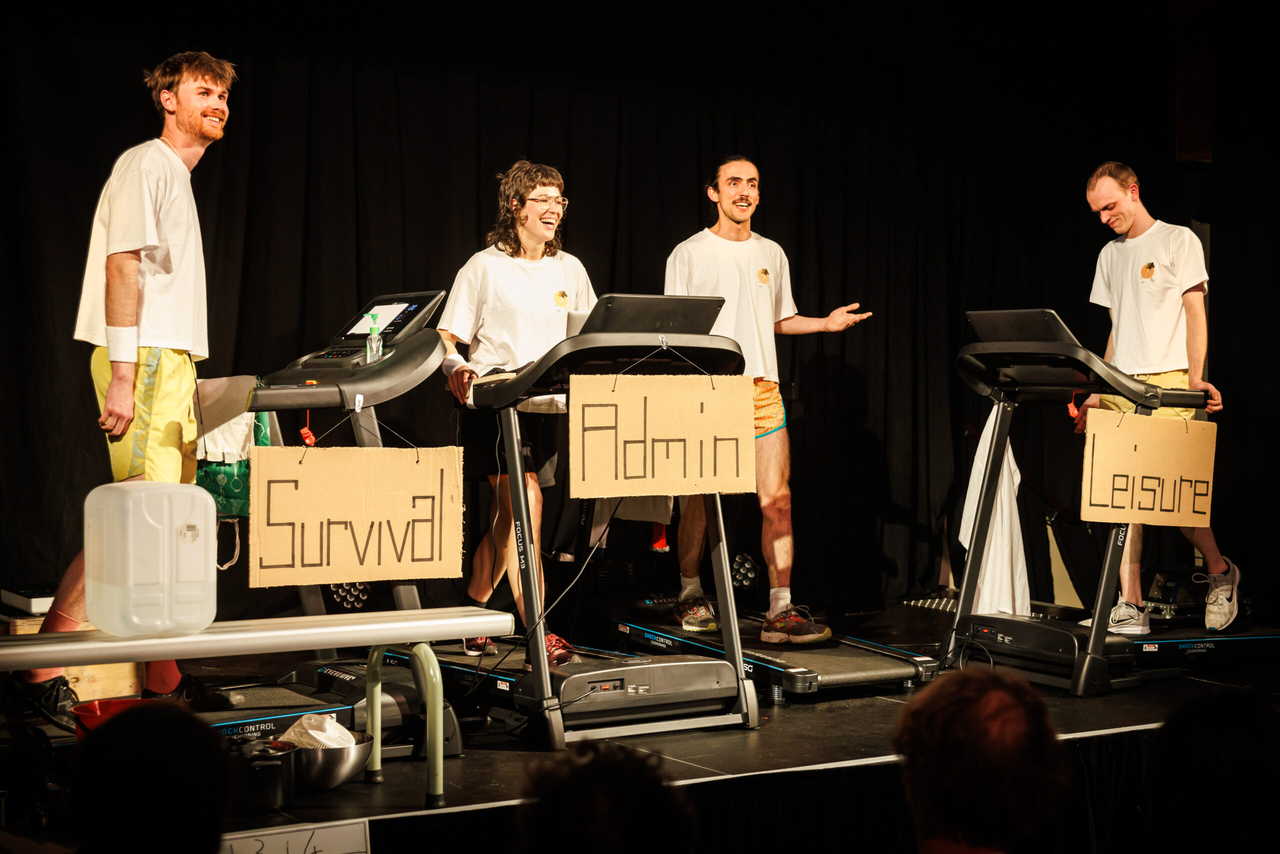 Four performers stand on treadmills on a stage.