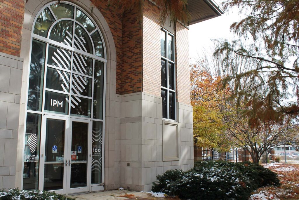 A brick and stone building with a large glass door and a large white logo covering the top half of the door. The logo looks like the map of Illinois but filled with stripes that look like a fingerprint.