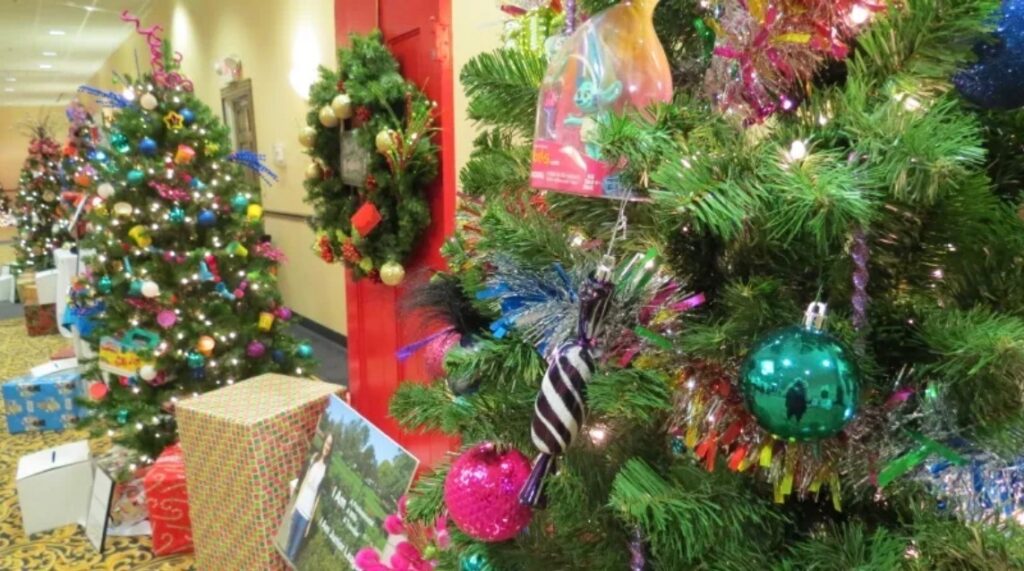 A box covered in wrapping paper, two trees and a wreath decorated for Christmas on display.