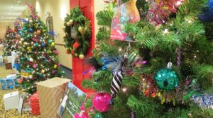 A box covered in wrapping paper, two trees and a wreath decorated for Christmas on display.