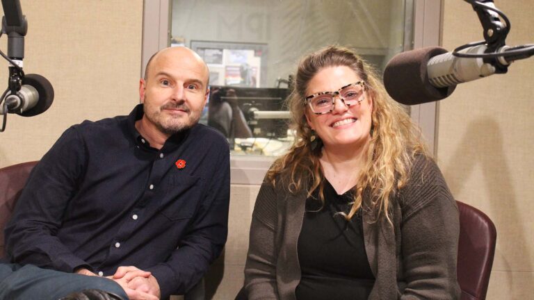 A white man and a white woman smile for the camera in a radio studio.