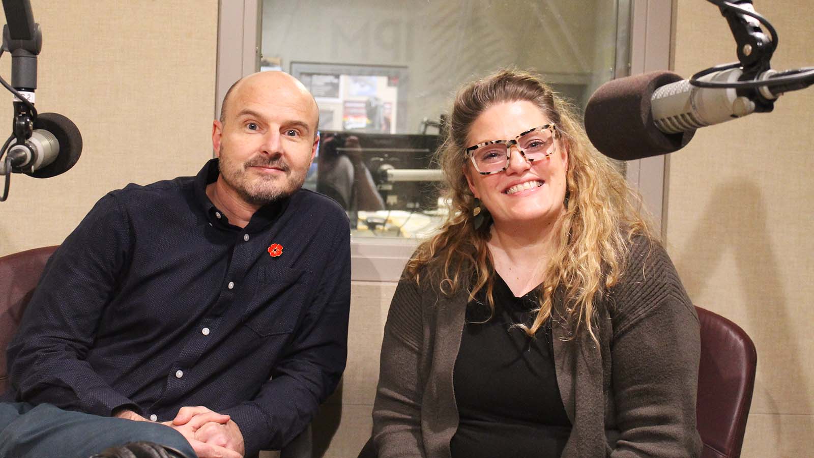 A white man and a white woman smile for the camera in a radio studio.