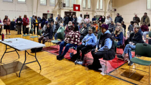 A group of people are seated inside the former National Armory in Champaign