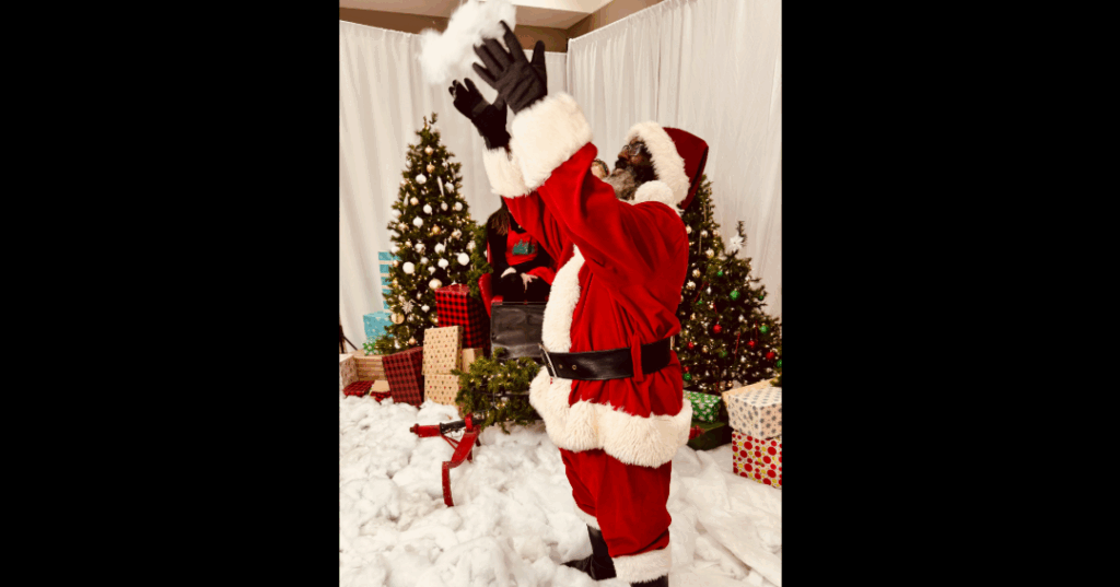 A man dressed in a red and white suit as Santa Claus plays with fake snow.