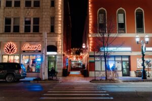 Lights line an alleyway between two storefronts and in front of a road.