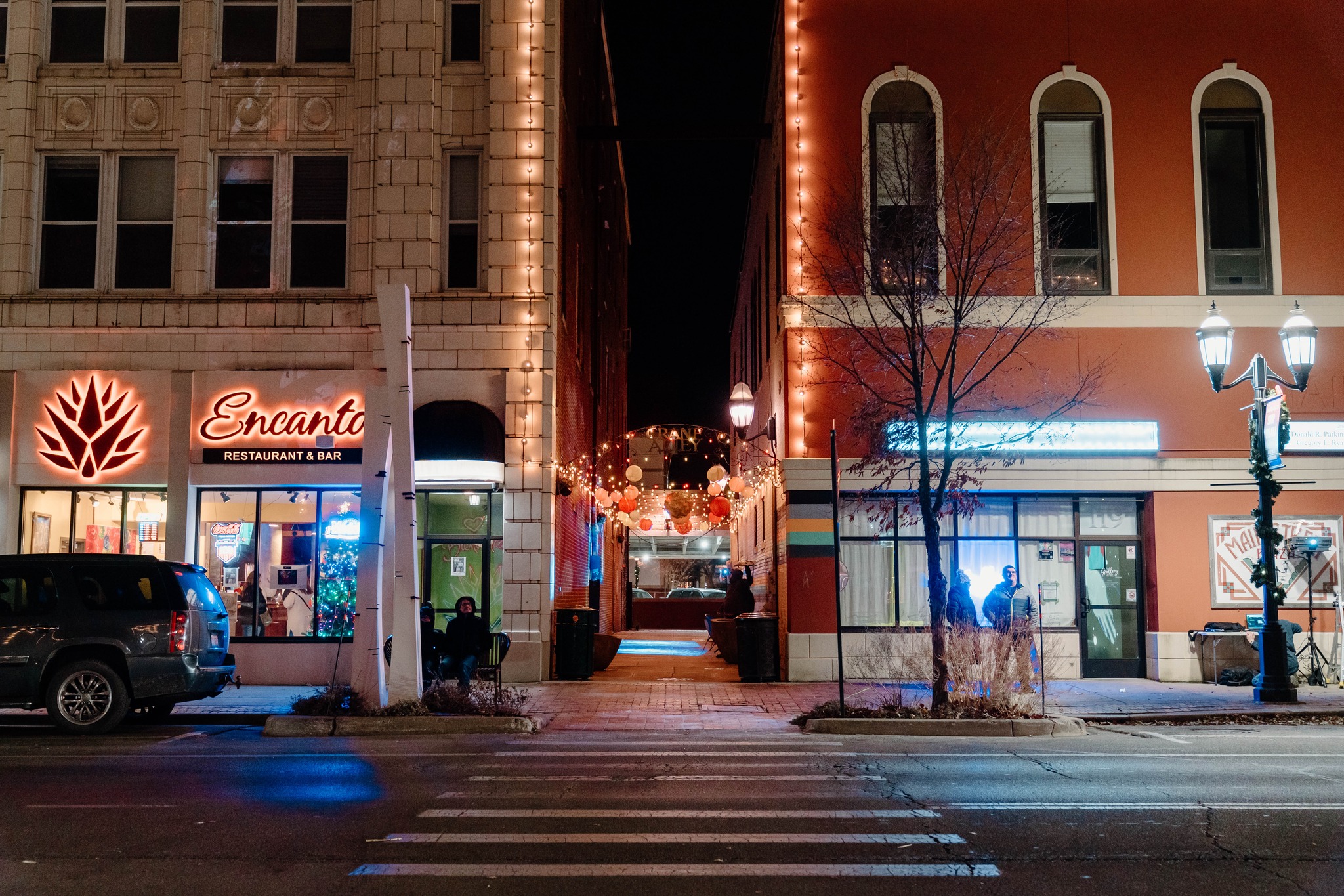 Lights line an alleyway between two storefronts and in front of a road.