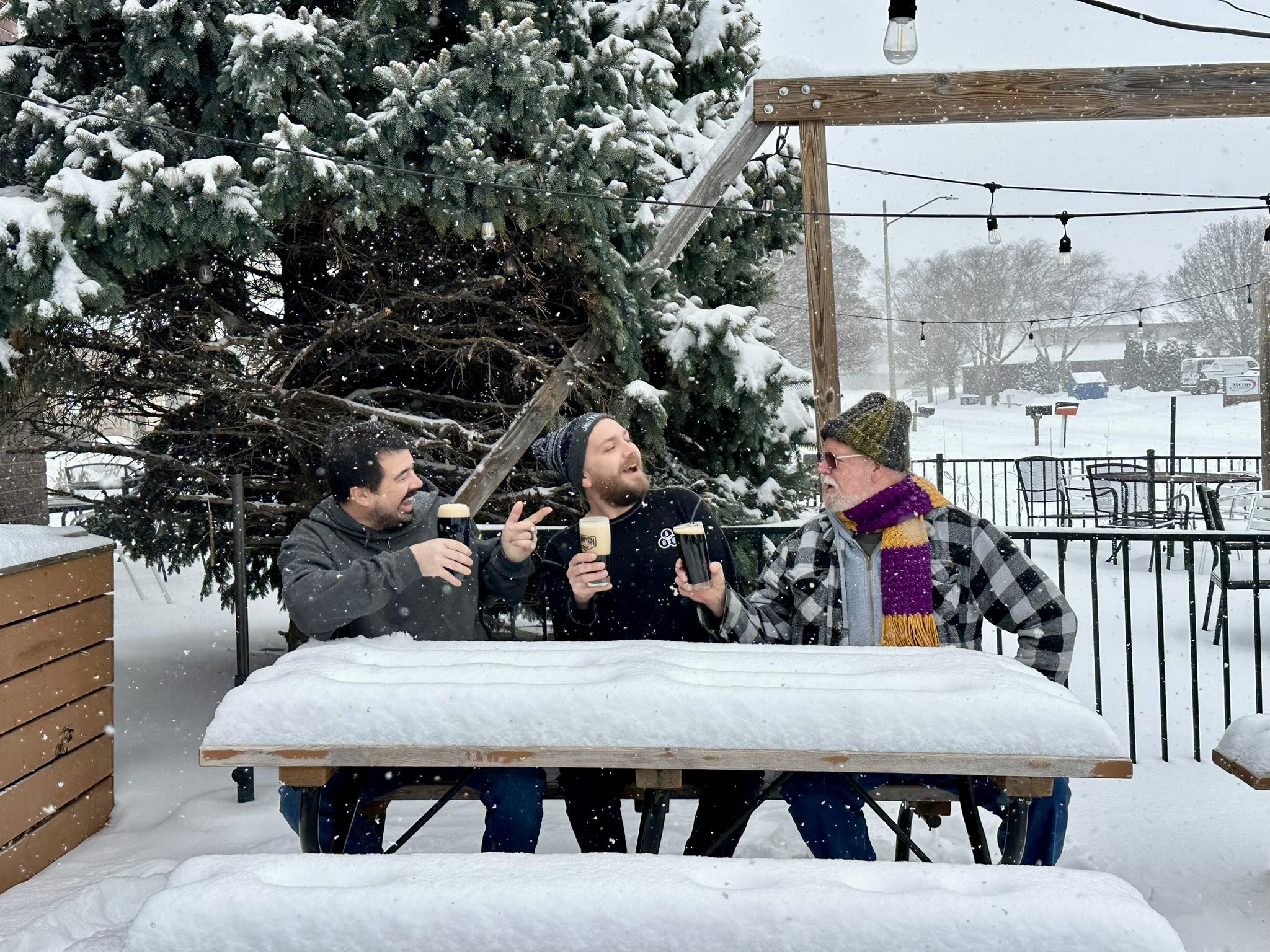 Three people drink from pint glasses in the snow.