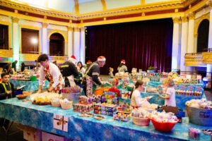 Children and adults surround tables full of items in a theater