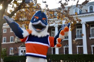 Someone wears a blue and orange Kingfisher outfit and stands with their arms out in front of the Illini Union.