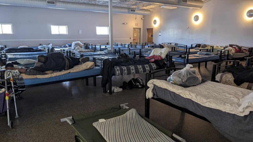 people laying on beds inside a homeless shelter