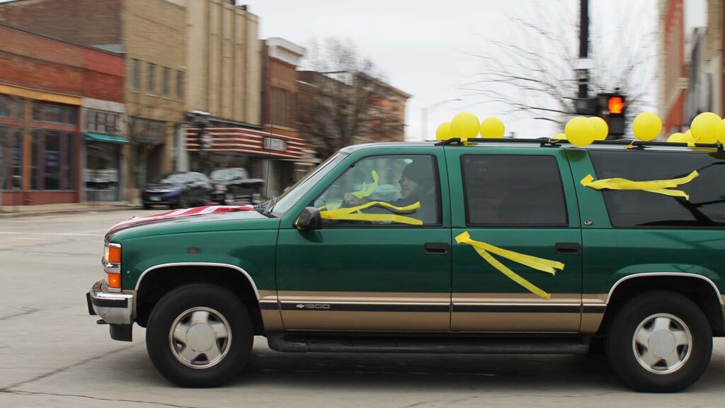 A green car with yellow streamers and yellow balloons turns at a stoplight in downtown Urbana.