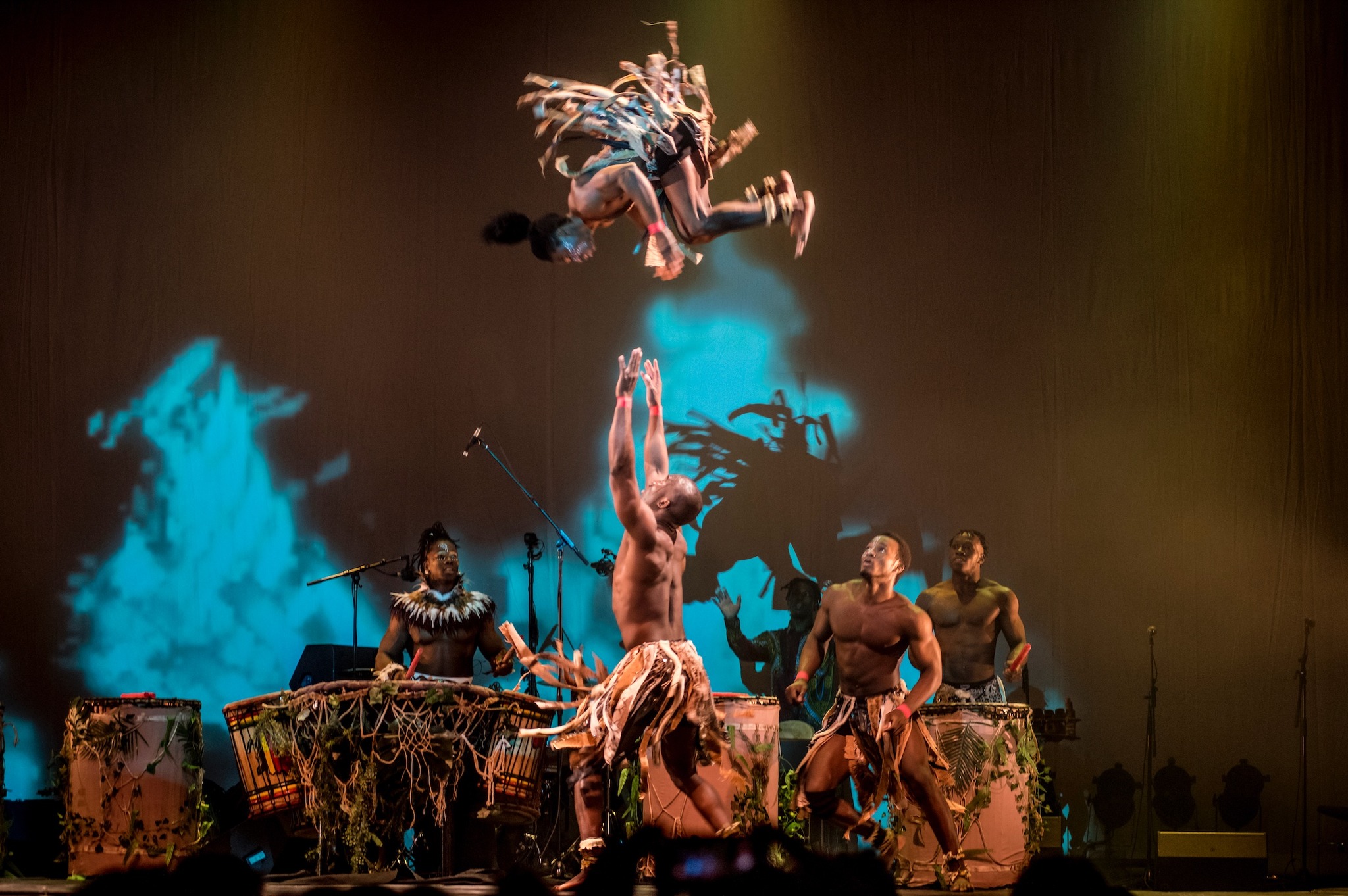 A man somersaults in the air over other performers on stage.