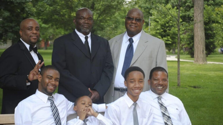 Three men in suits stand behind four younger men in dress shirts and ties.